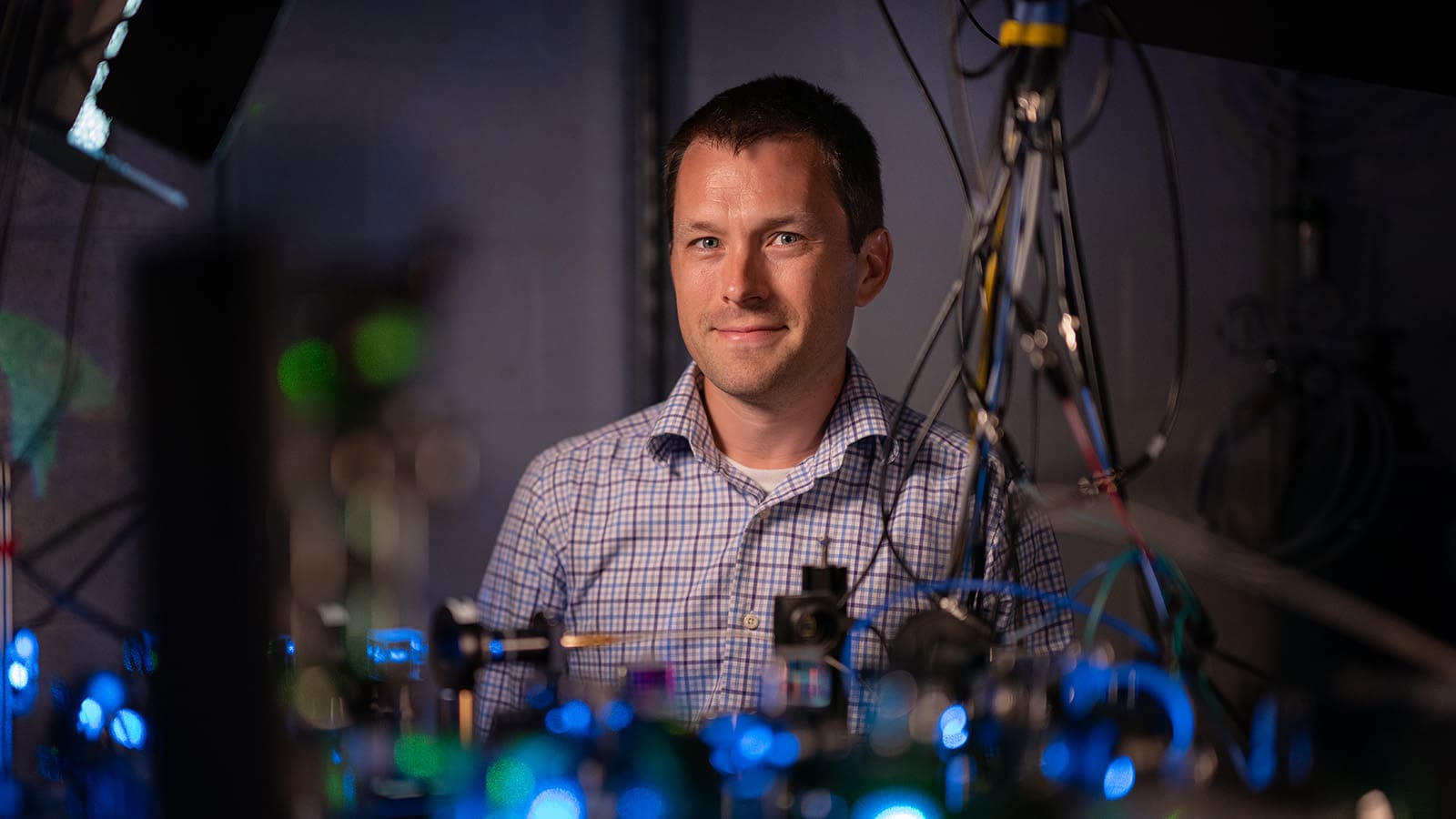 Portrait in lab, dark environment with blue/green glowing objects
