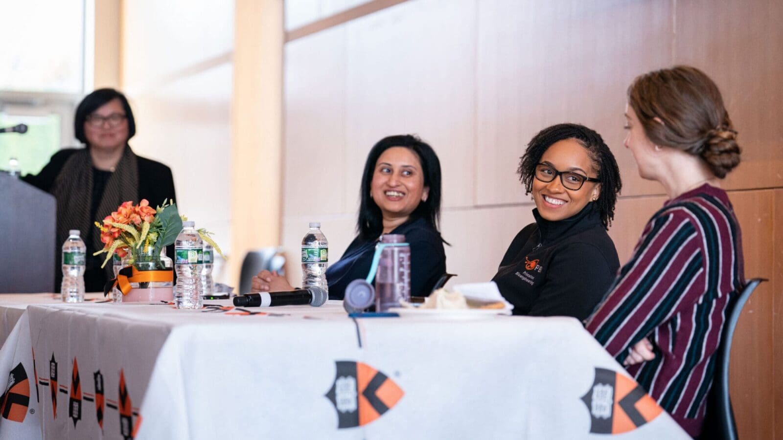 Three panelists sit at a table, interacting and smiling