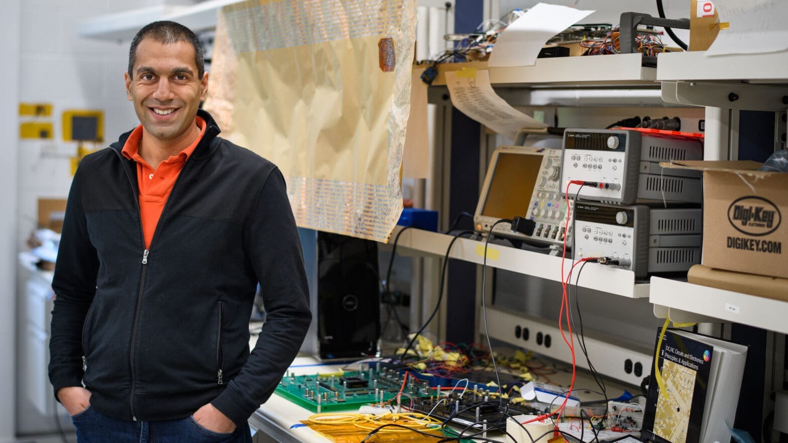 Verma posing in his lab with technical equipment.