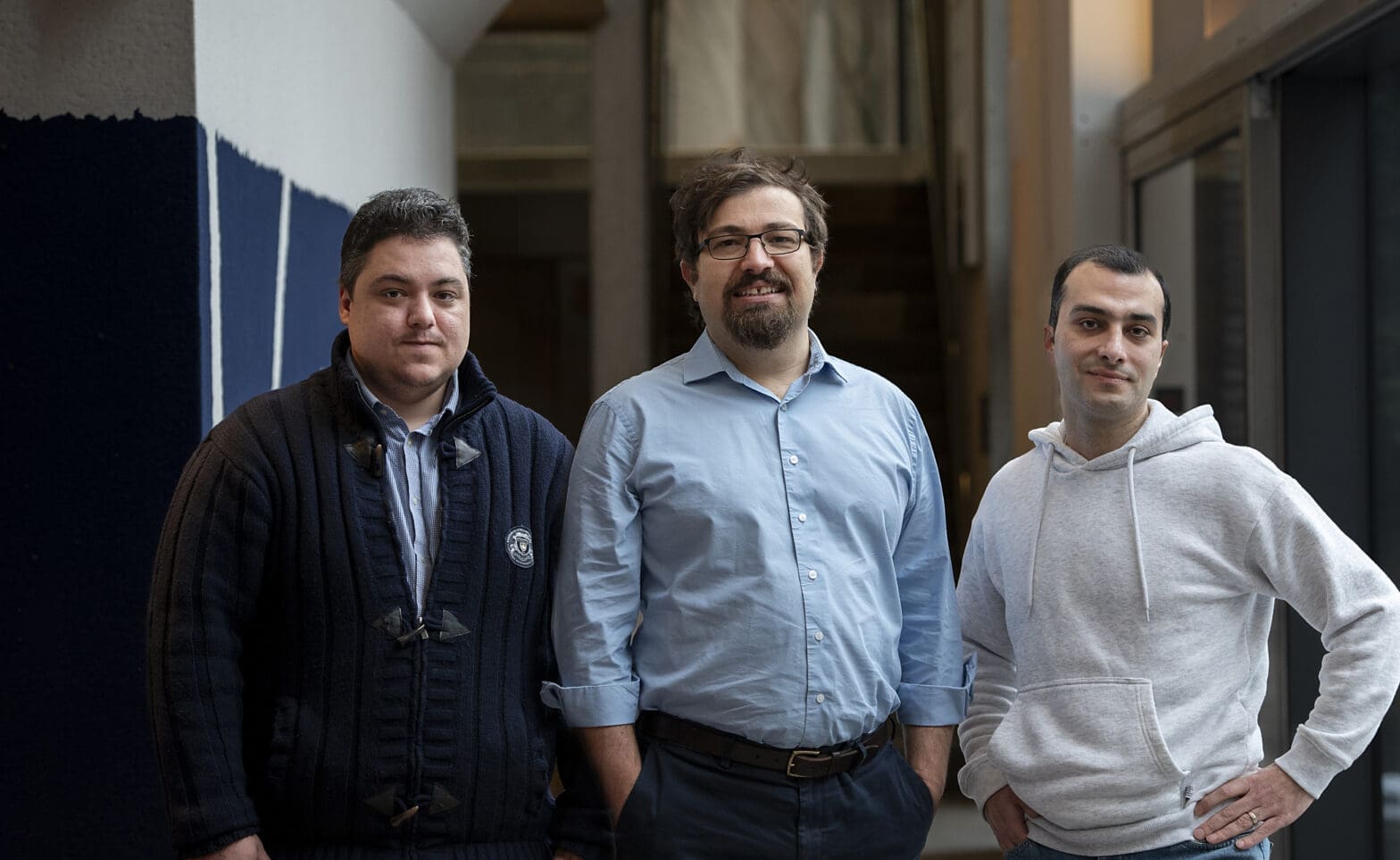 Three men stand in a hallway.
